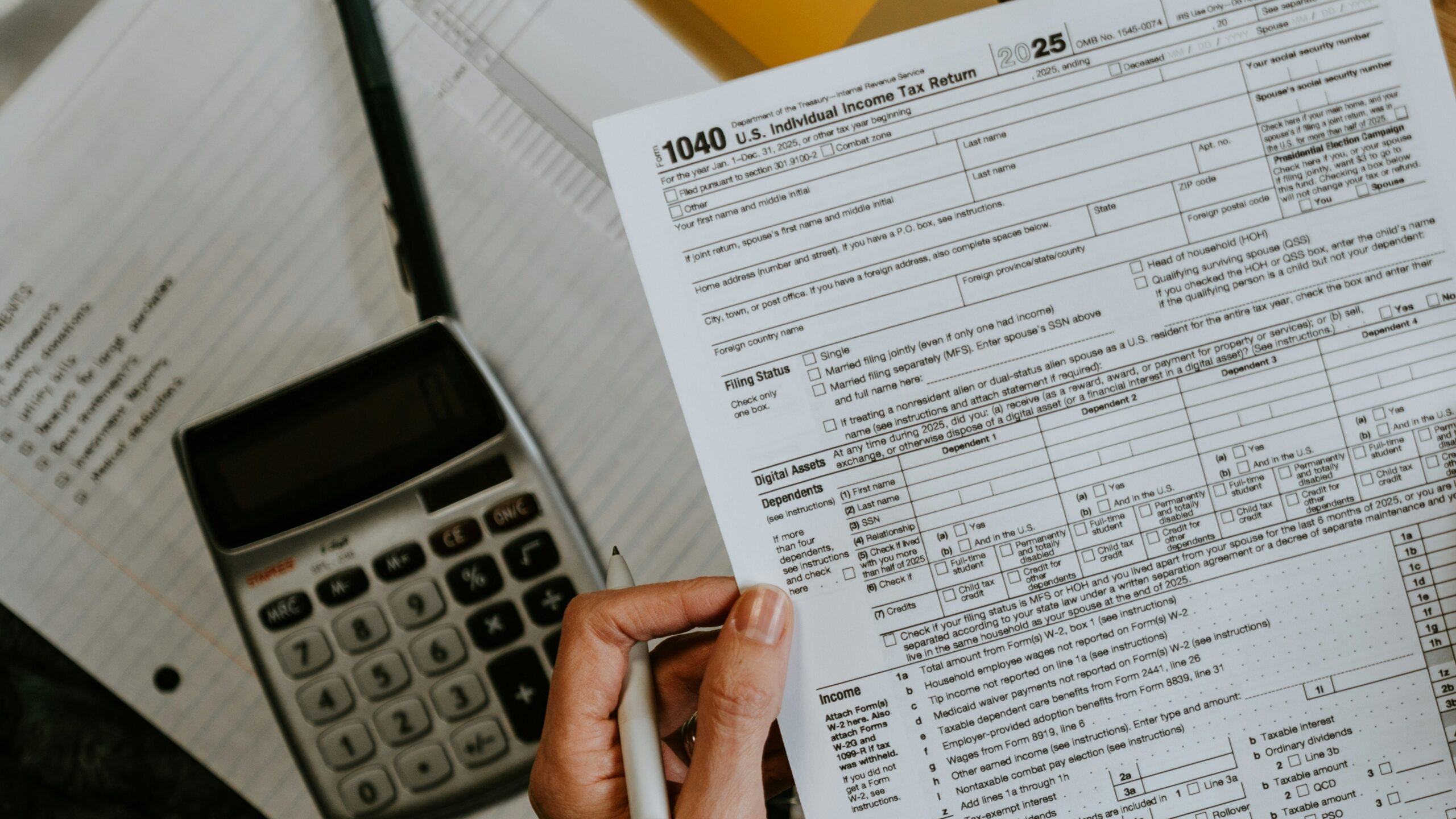 Hands holding tax forms with calculator and laptop.