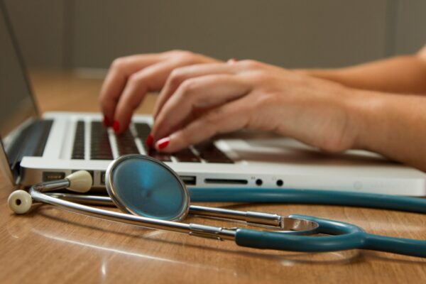 person sitting while using laptop computer and green stethoscope near