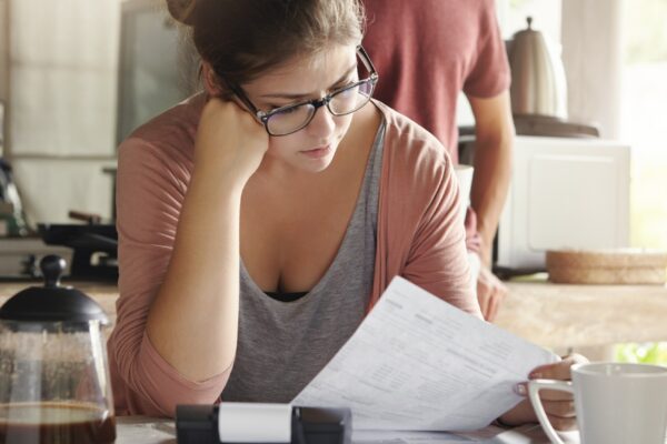 Family budget and finances. Serious woman doing accounts and feeling frustrated with amount of monthly expenses. Young female wearing glasses calculating utility bills, sitting at kitchen table