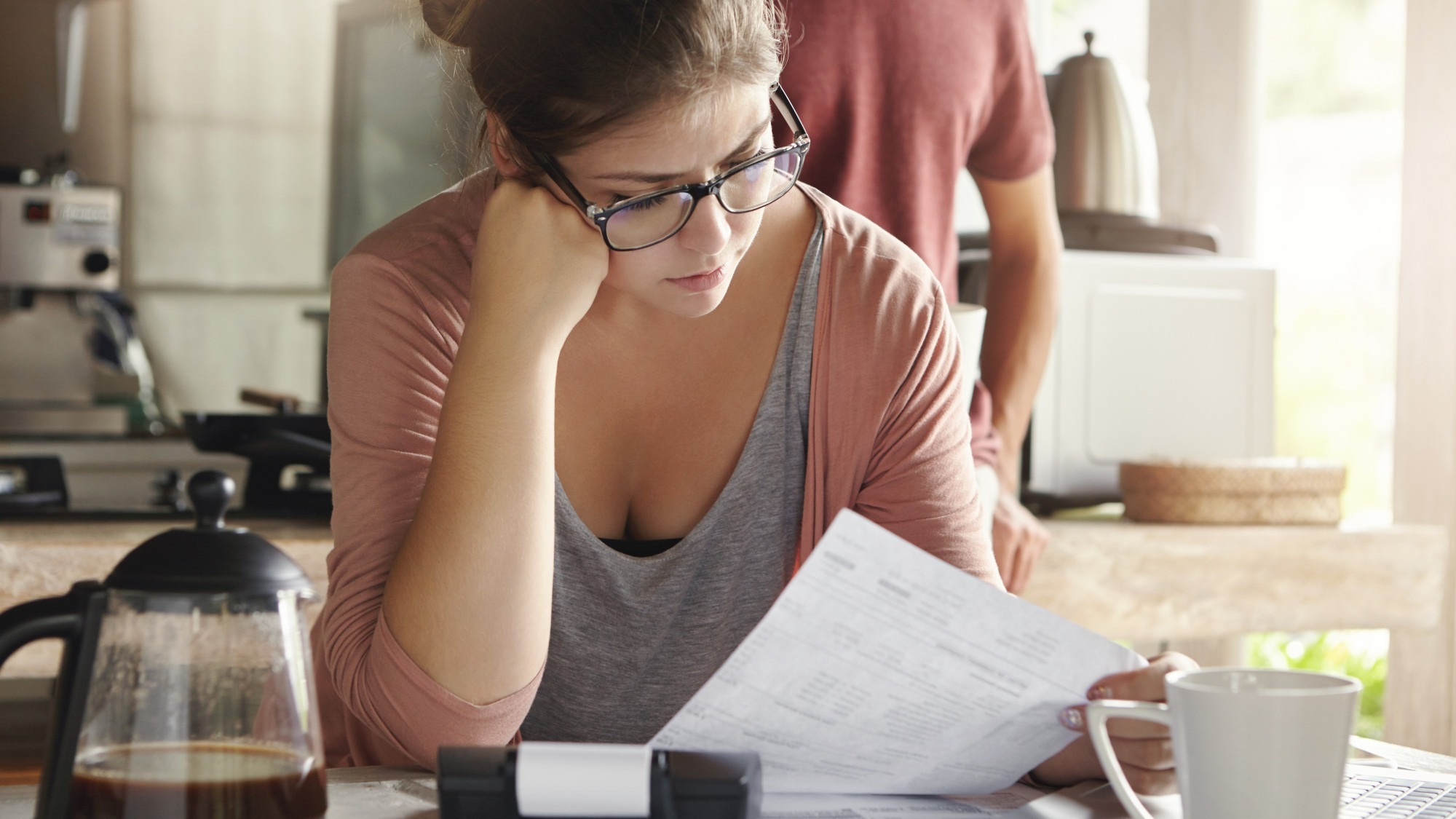 Family budget and finances. Serious woman doing accounts and feeling frustrated with amount of monthly expenses. Young female wearing glasses calculating utility bills, sitting at kitchen table