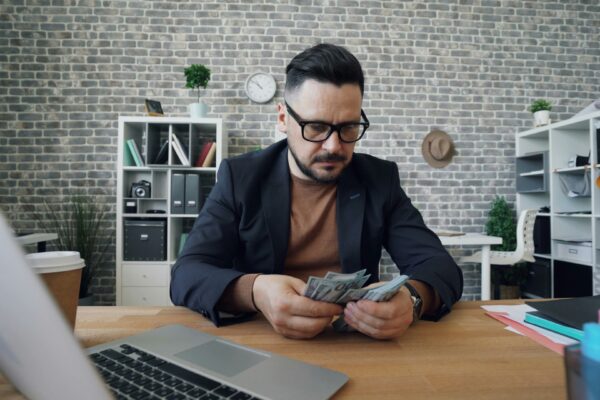 a man sitting at a table with a laptop and money