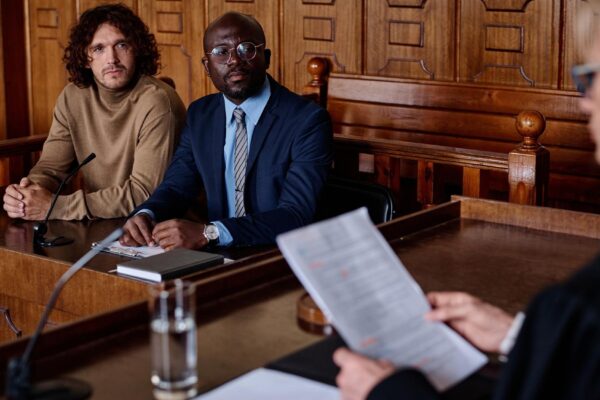 Two young intercultural male attorneys looking at female judge with paper documents