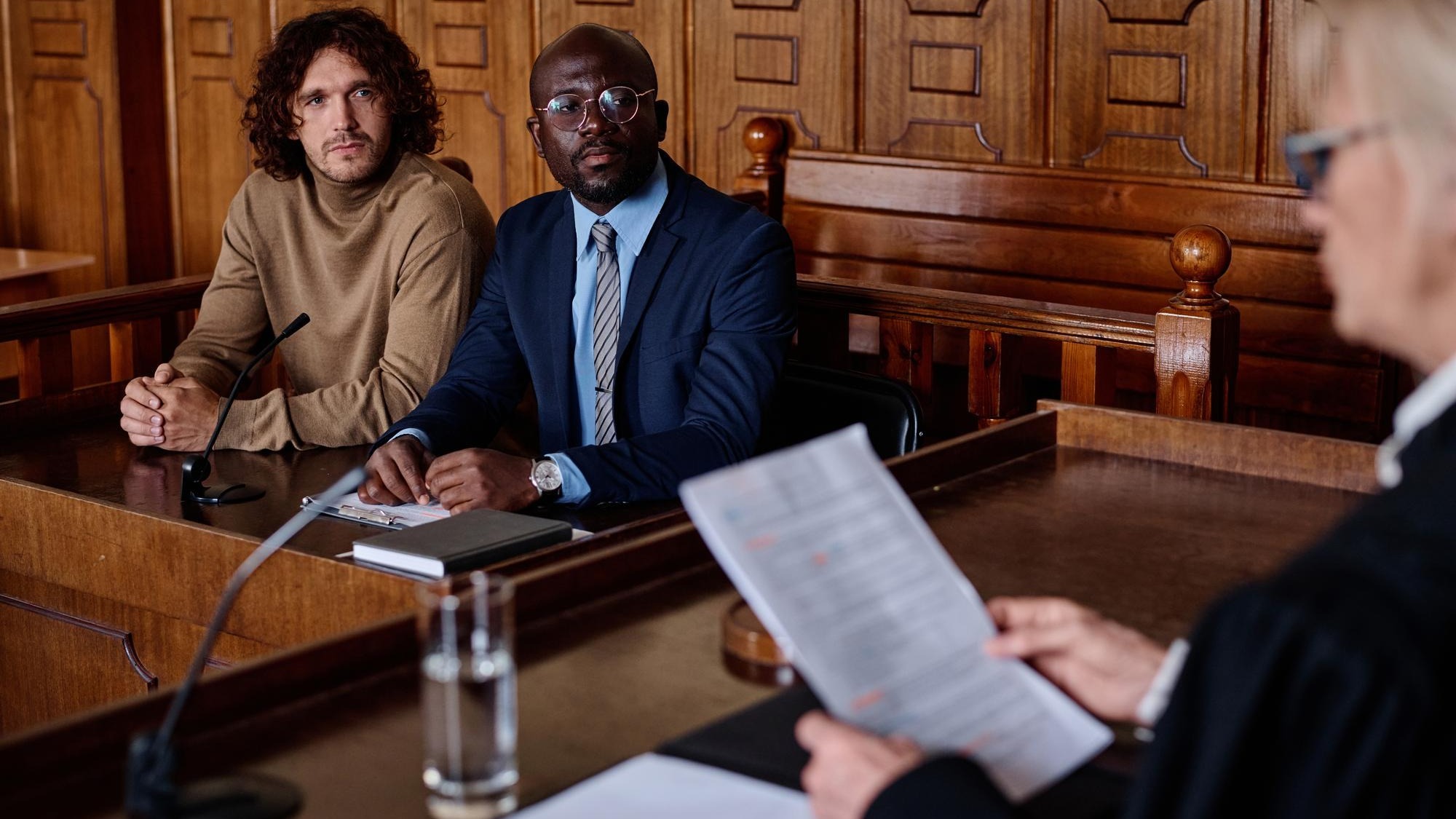 Two young intercultural male attorneys looking at female judge with paper documents