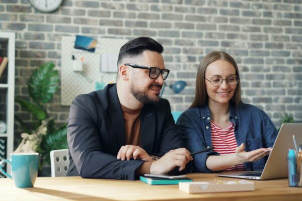 a man and a woman sitting at a table looking at a laptop