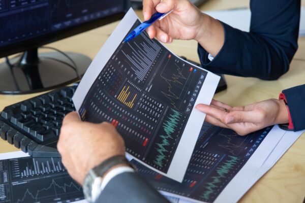 Brokers discussing trading strategy, holding papers with financial data, pointing pen at charts. Cropped shot. Broker job or stock market exchange concept