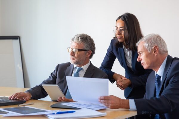 Concentrated partners using laptop and working with documents. Confident serious businesspeople in office suits discussing company project together. Management, business and partnership concept