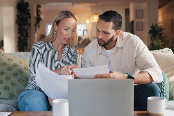 Home couple and laptop with talking for document financial bills and problem solving for budget Sofa woman and man with paperwork for tax deduction mortgage expenses or discussion in living room