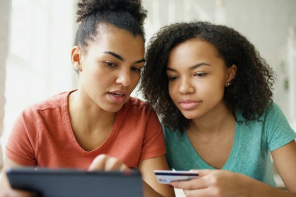 Two young women looking at a tablet with credit card.