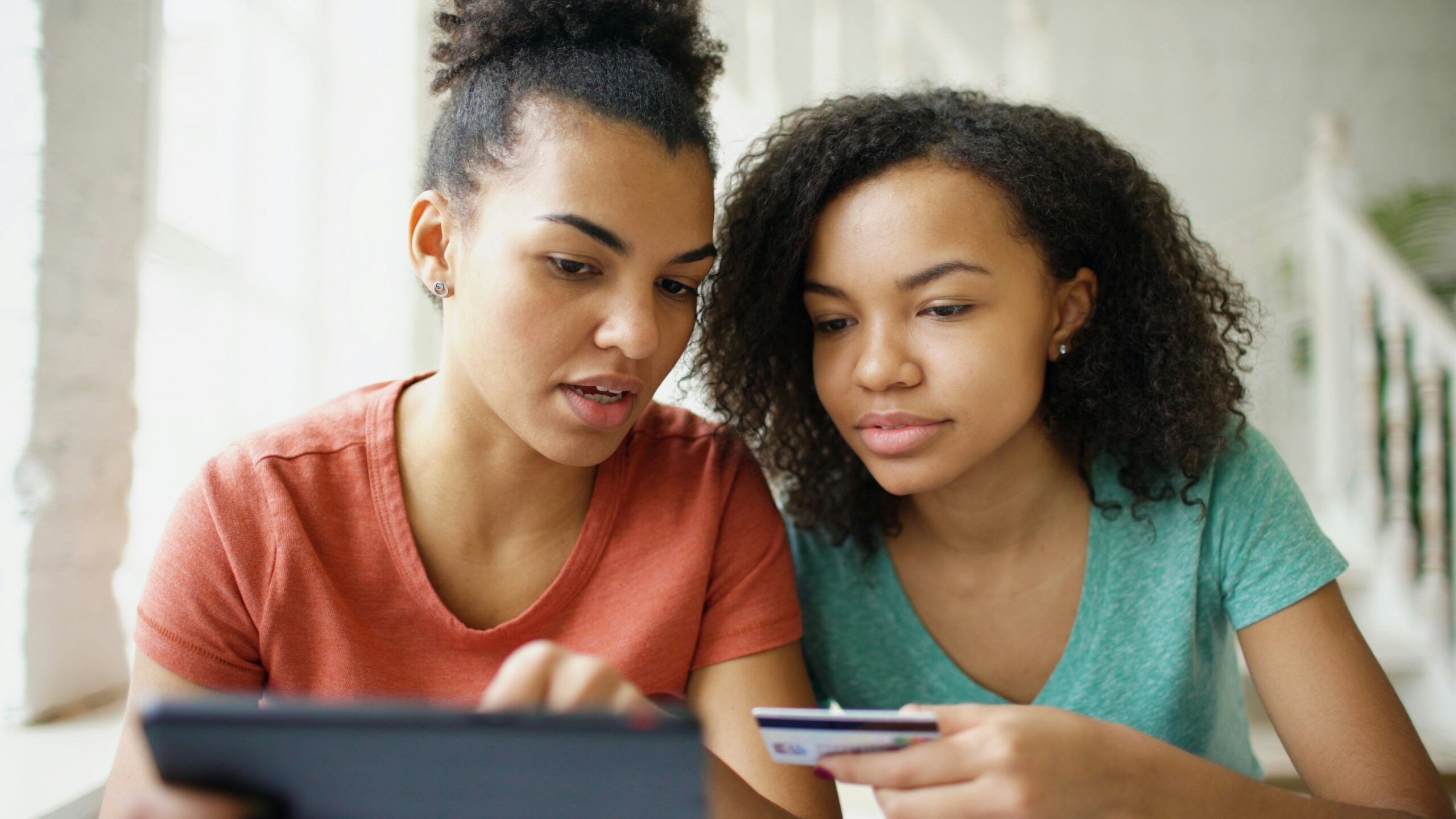 Two young women looking at a tablet with credit card.