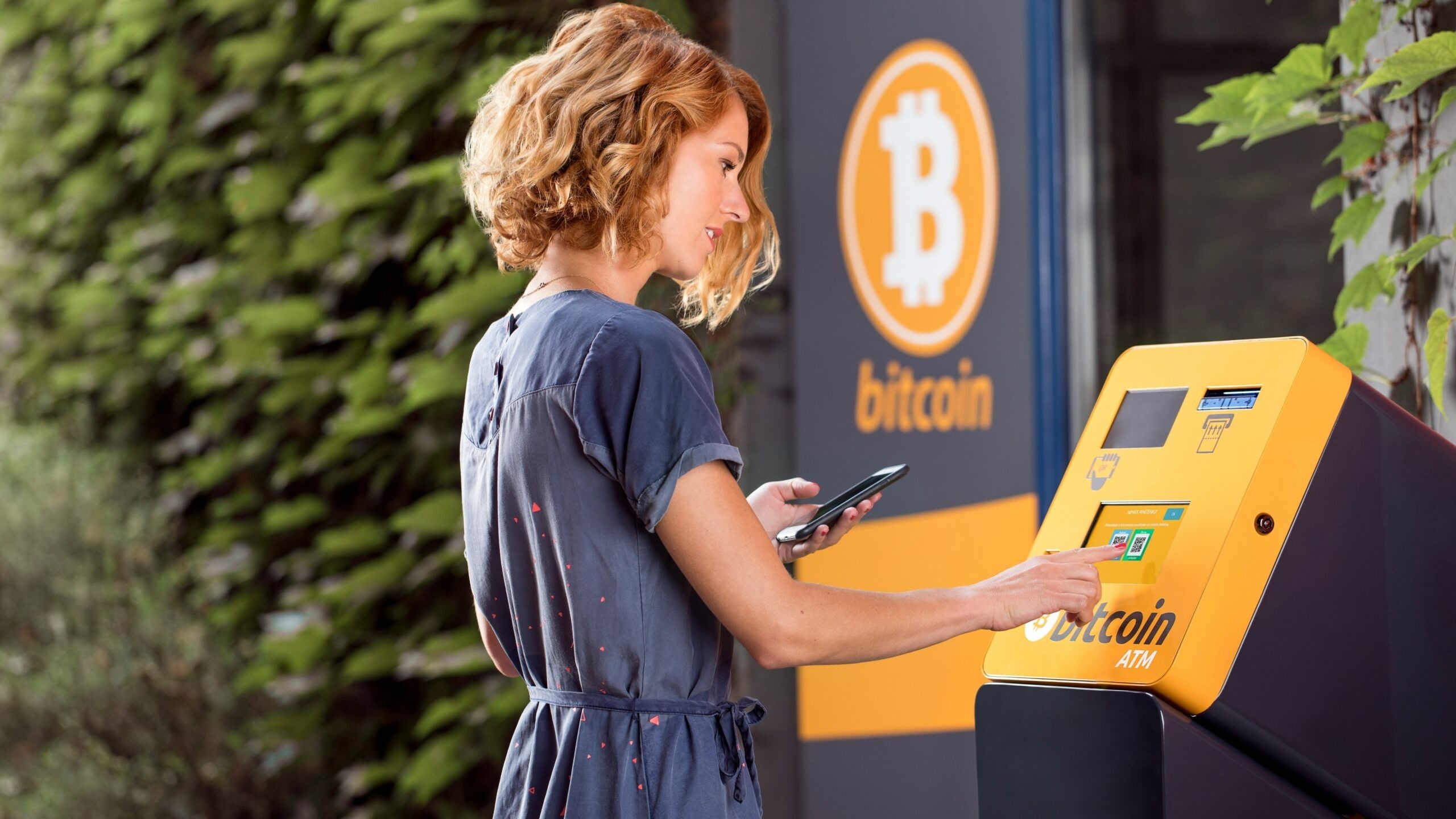 a woman using a cell phone in front of a bitcoin machine