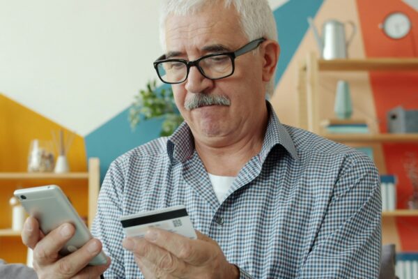 Elderly man using smartphone and credit card for online shopping.