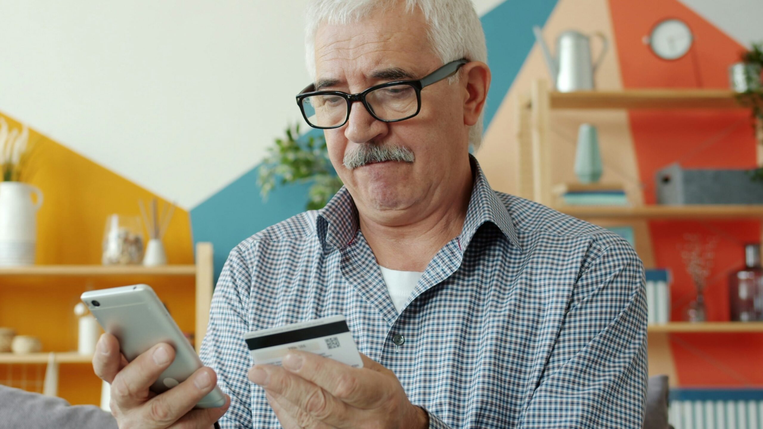 Elderly man using smartphone and credit card for online shopping.
