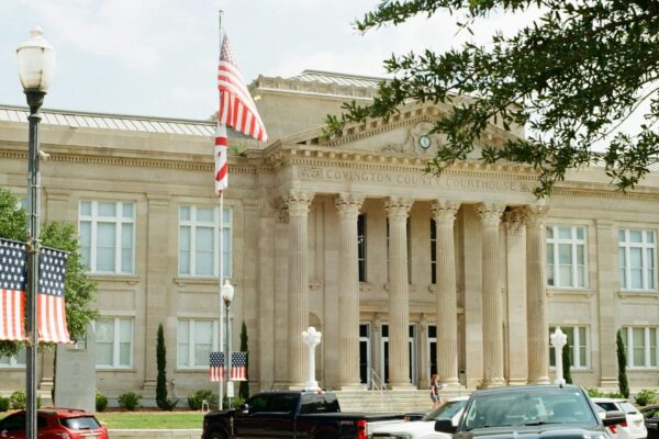 Classical building with columns, american flags, and parked cars.