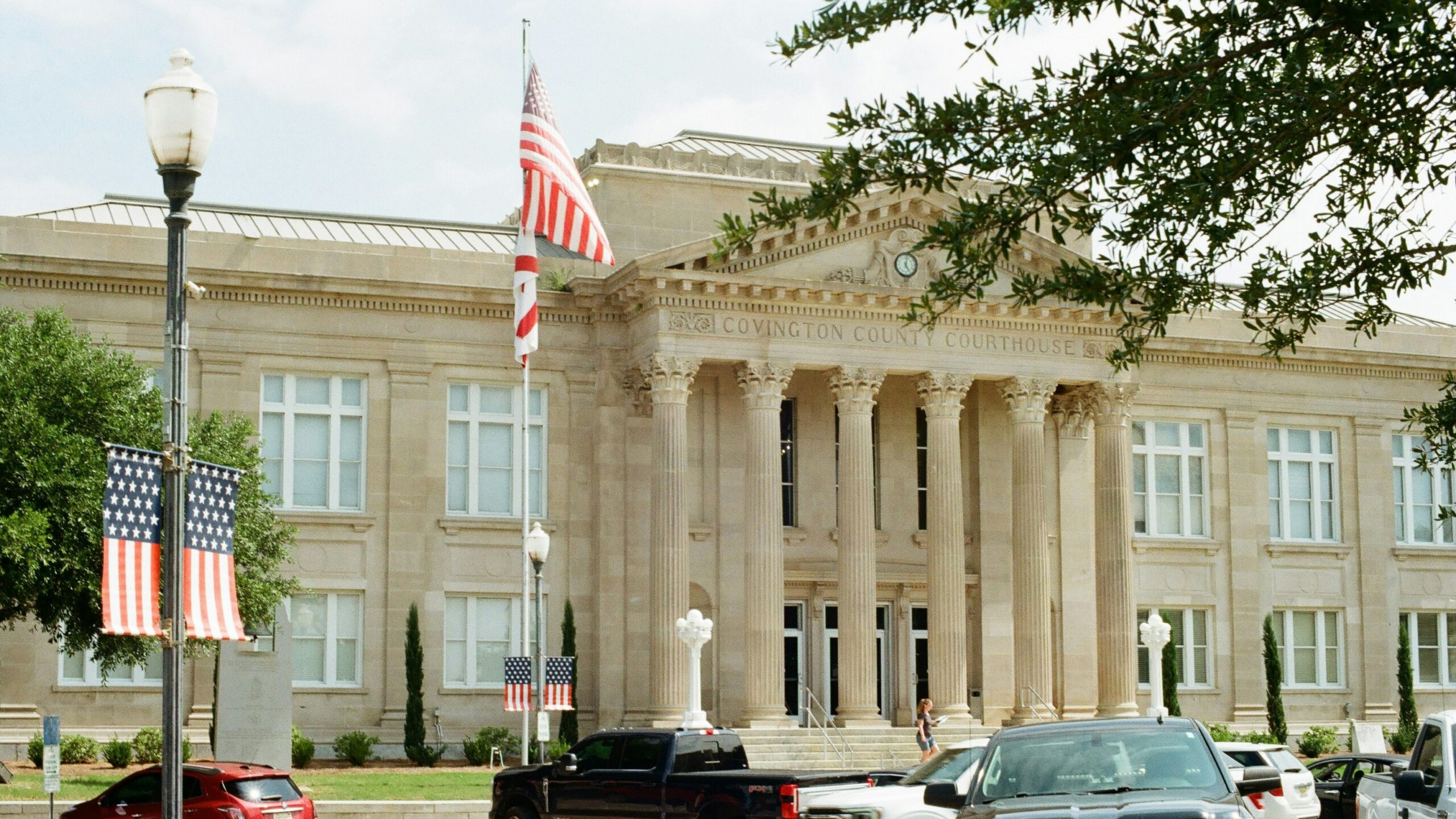 Classical building with columns, american flags, and parked cars.