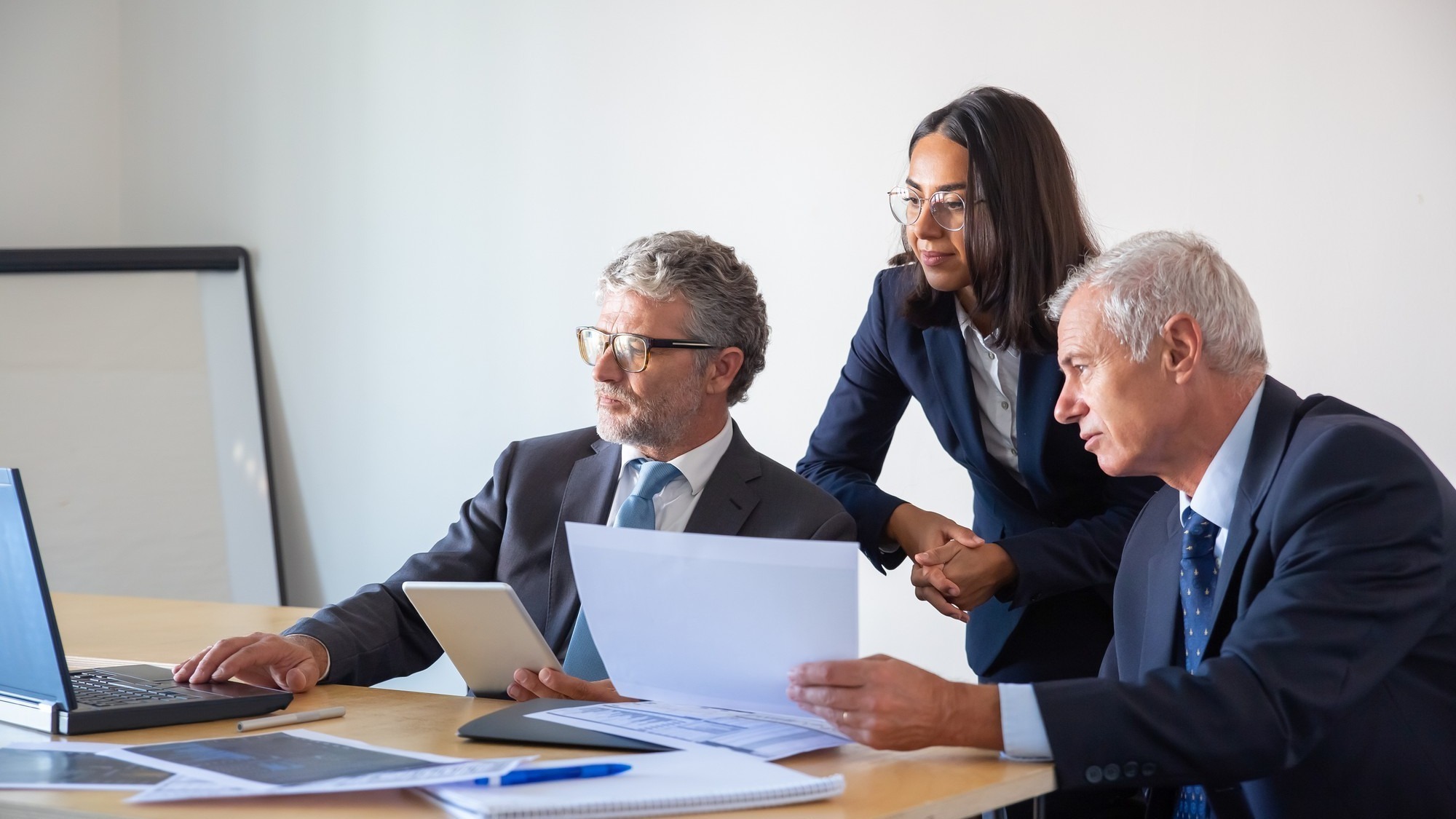 Concentrated partners using laptop and working with documents. Confident serious businesspeople in office suits discussing company project together. Management, business and partnership concept