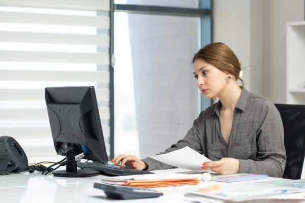 Young woman focused on computer and documents at office desk.