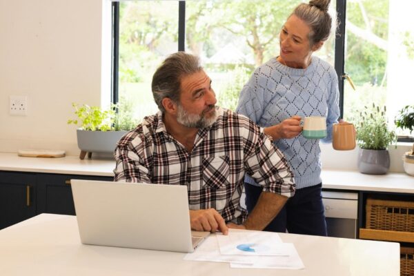 Mature couple enjoying coffee break at home man using laptop in kitchen