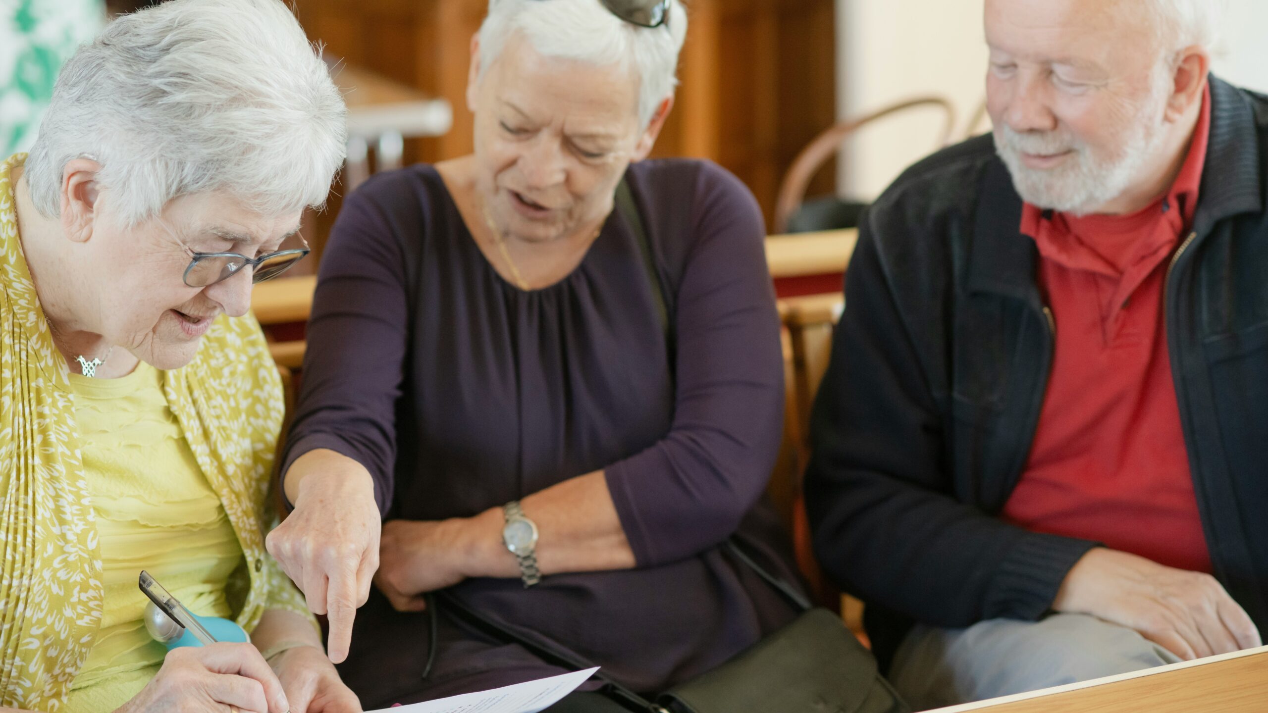 Three older adults are looking at a paper.