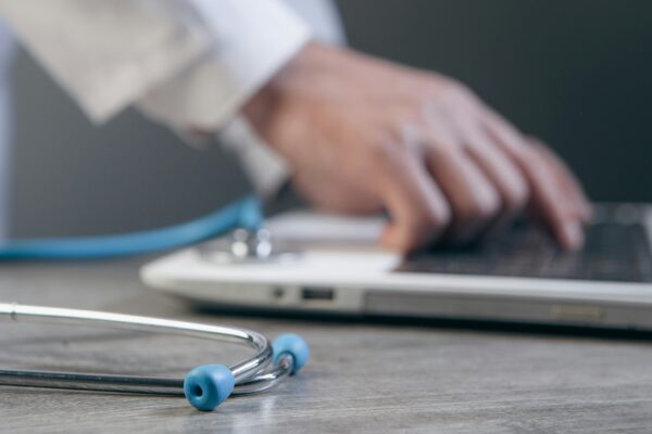 Doctor typing on a laptop with a stethoscope nearby.