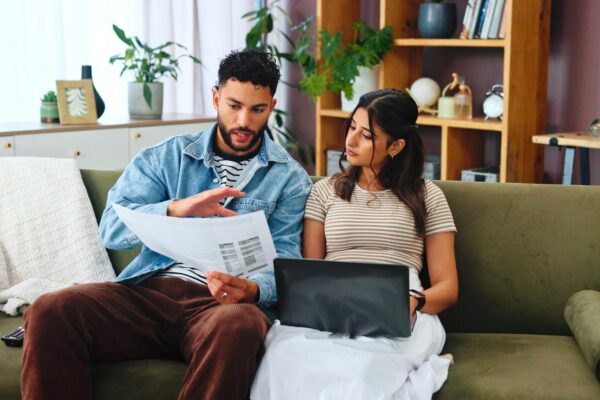 Documents laptop and couple on sofa in home for bills payment receipts and banking Marriage relationship and man and woman with paperwork for financial planning with taxes insurance and budget