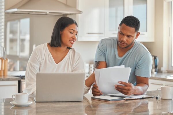 Couple laptop and paper in home for discussion online banking and travel budget Man woman or document in kitchen with tech invoice payment or explain contract for property investment opportunity