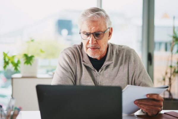 Laptop documents and mature businessman in office with finance report for company budget planning Research paperwork and financial manager with investment proposal for stock market in workplace