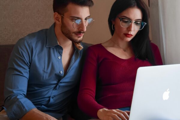 A man and woman sitting on a couch looking at a laptop