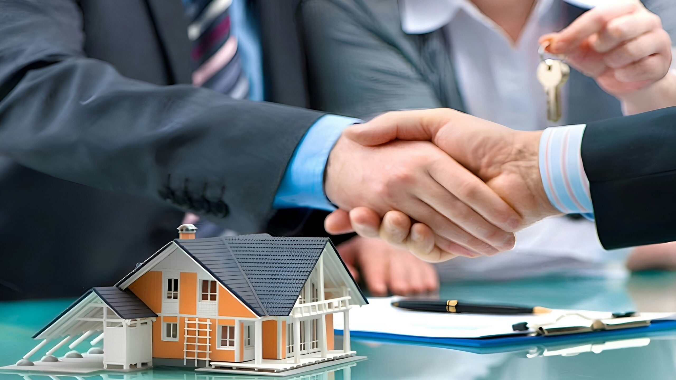 Two men shaking hands over a house model and keys.