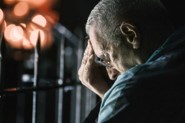 Elderly man with hand on forehead at night.
