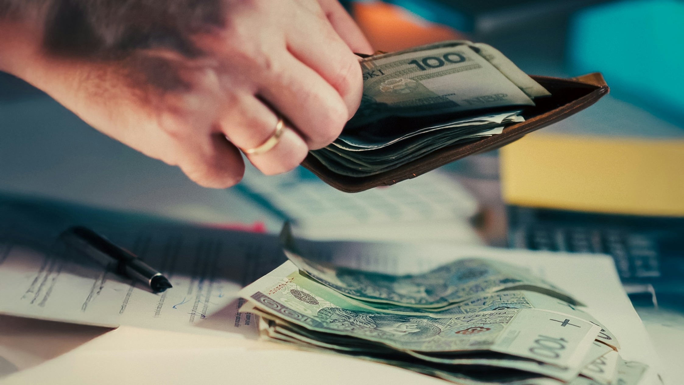Hands counting money from a wallet over papers.