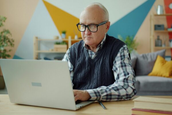 Elderly man wearing glasses using a laptop at home.