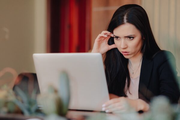 Young attractive emotional girl in business-style clothes sitting at a desk on a laptop