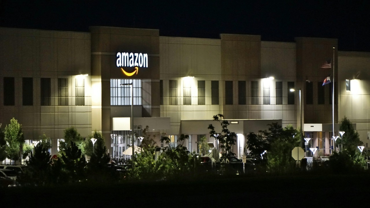 Amazon warehouse building illuminated at night with trees and signage.