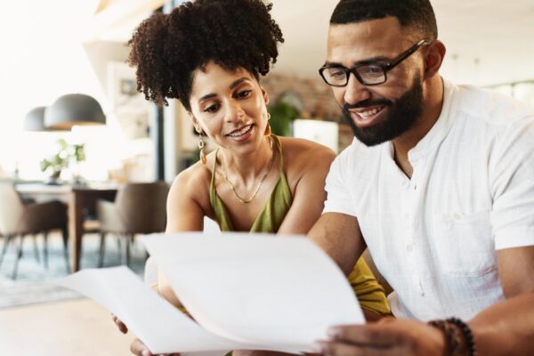 Couple paperwork and couch in home with investment budgeting and financial notes for saving Smile insurance and payment report with happy people together with documents for finance planning