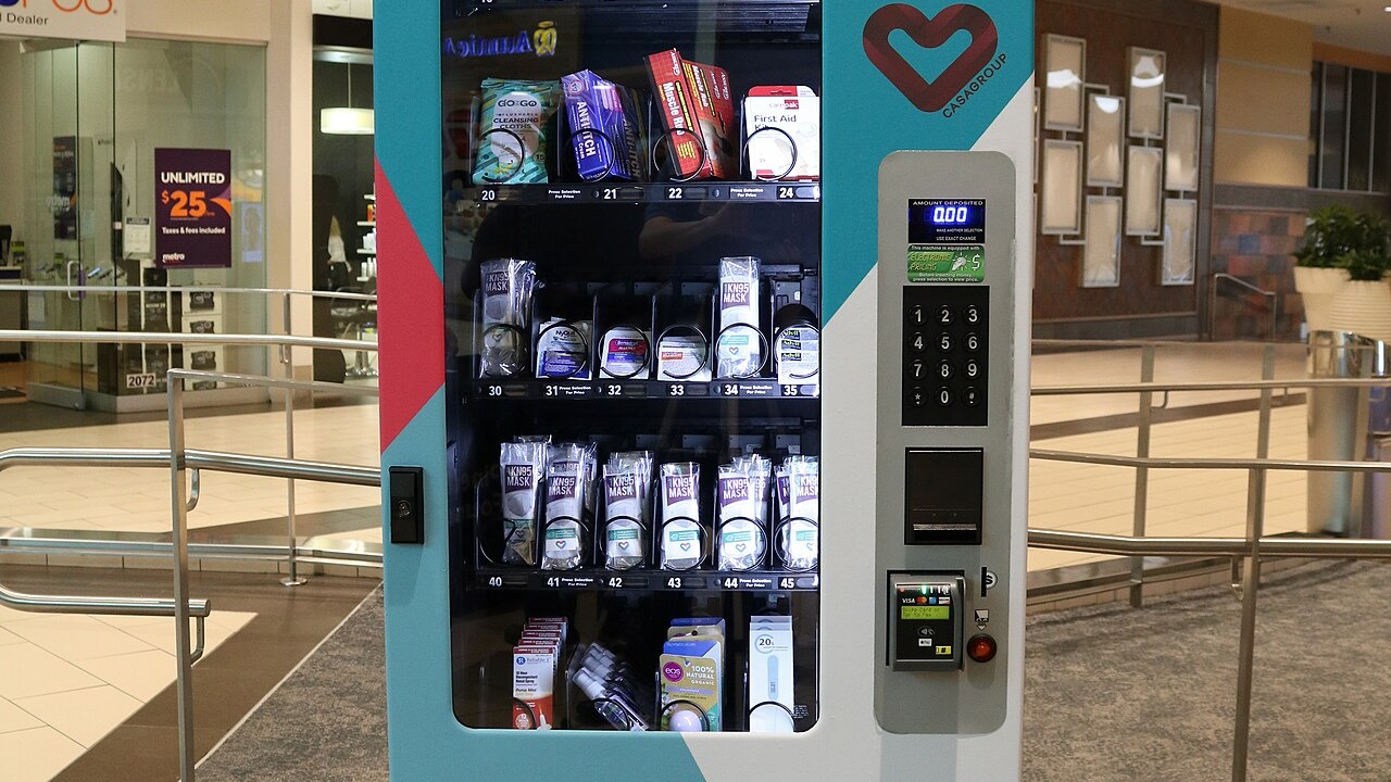 Front view of a CasaGroup (Casa Group) Pharmachine vending machine in the Westfield Countryside shopping mall in Clearwater, Florida. Items visible from inside the machine include toothbrushes and toothpaste; anti-itch cream; Assured muscle rub gel; Carepak travel-size first aid kits; KN95 face masks; NyQuil, Benadryl, Motrin, and Advil products; decongestant nasal sprays; A Gift From Nature hand sanitizer; EOS lip balm; and thermometers.