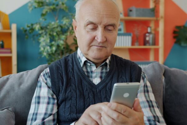 Elderly man using a smartphone on a couch.