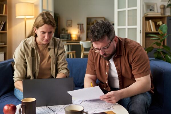 Caucasian young adult man and woman reviewing financial papers while paying taxes