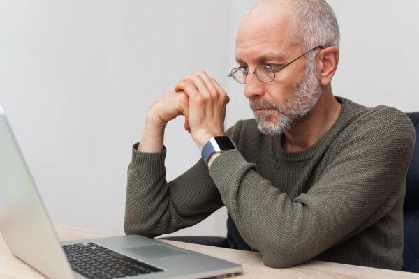 Adult, pensive man with gray hair working on laptop