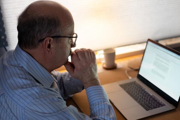 technology, oldness and lifestyle concept. Senior man in eyeglasses working with laptop computer at home and thinking on document.