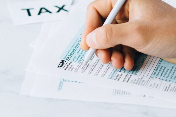 Hand completing tax forms with a pen, symbolizing financial deadline and time urgency.