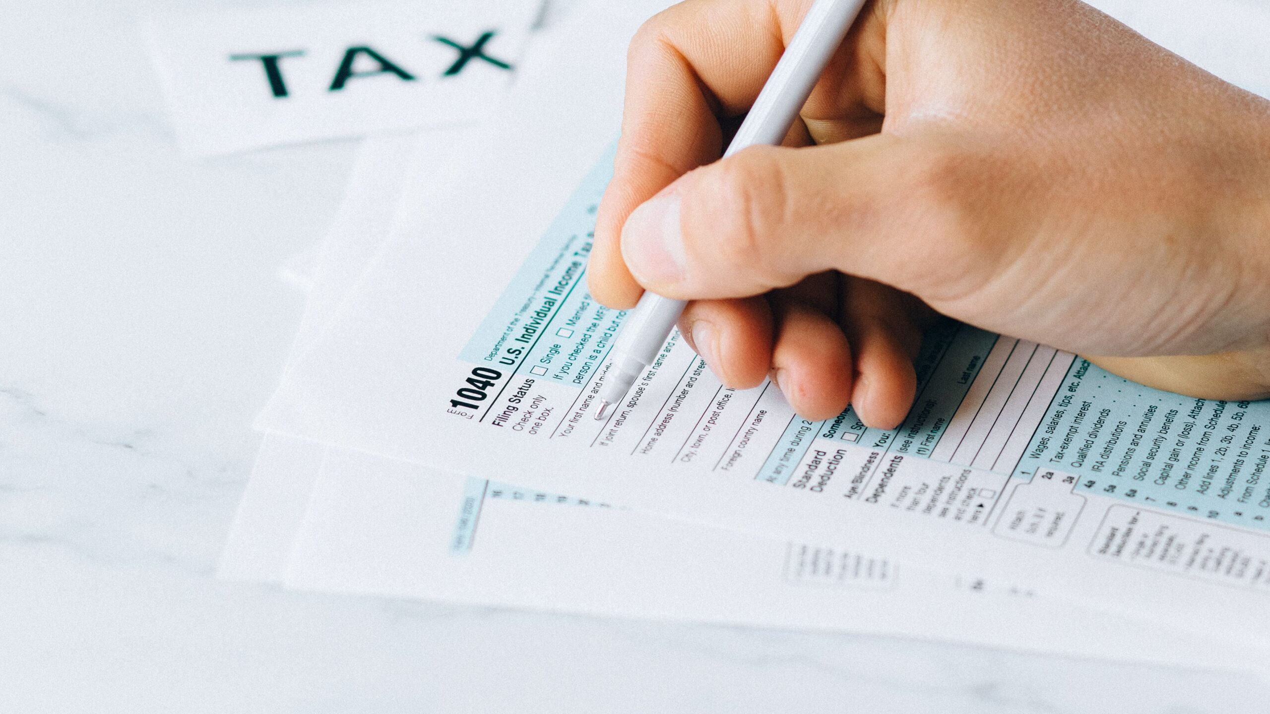 Hand completing tax forms with a pen, symbolizing financial deadline and time urgency.