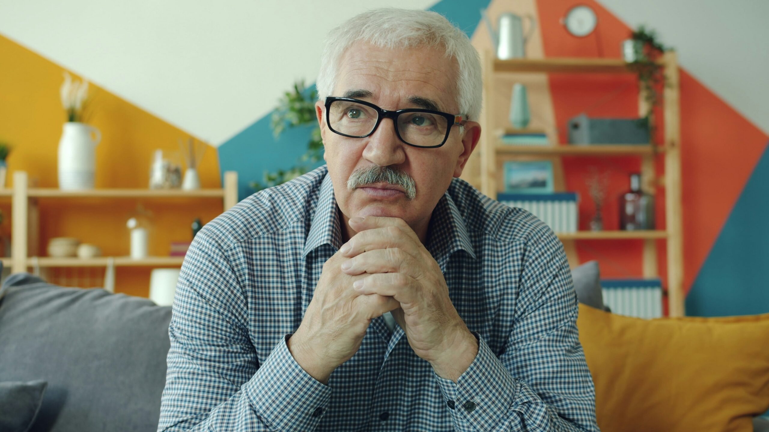 Elderly man with glasses resting chin on hands.