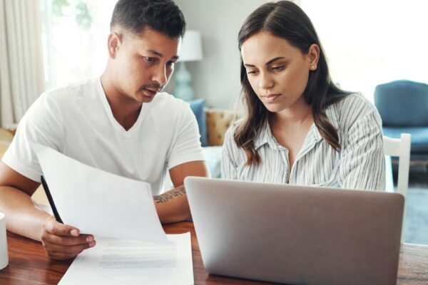 Couple conversation and paperwork with laptop in home for asset management savings fund and budget review Computer man and woman with mortgage research financial discussion and documents for tax