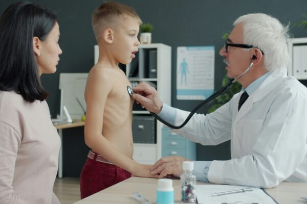 Doctor examines a young boy's chest with stethoscope.