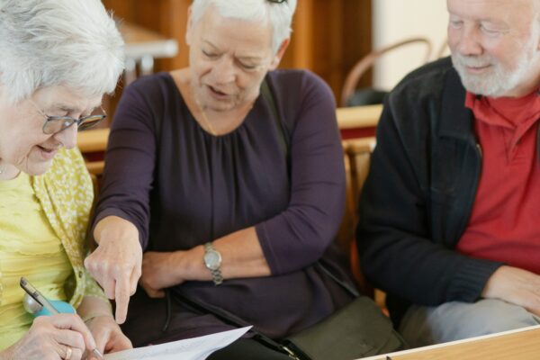 Three older adults are looking at a paper.
