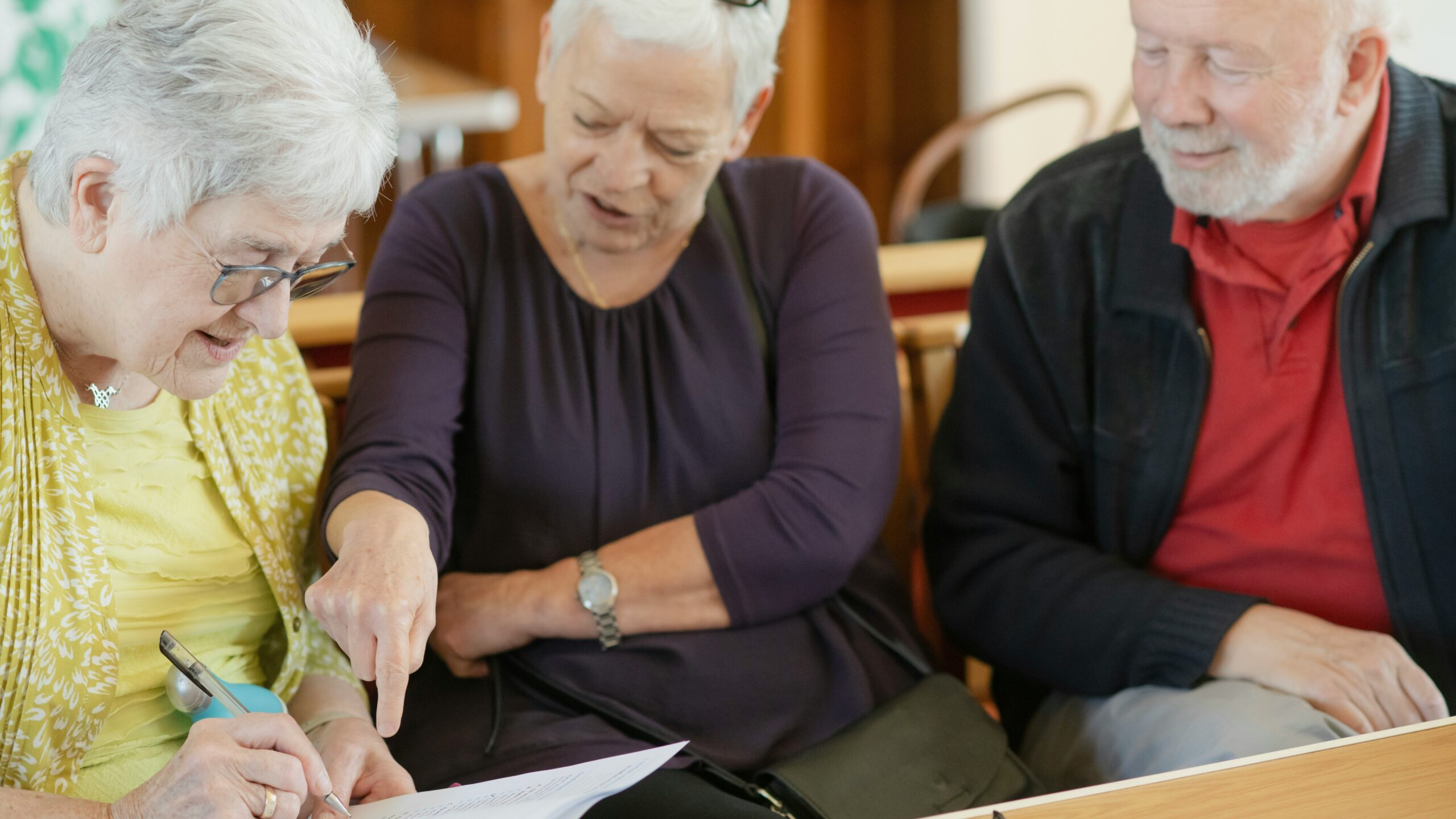 Three older adults are looking at a paper.
