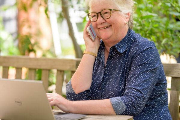 a woman on her phone while sitting at a table with a laptop