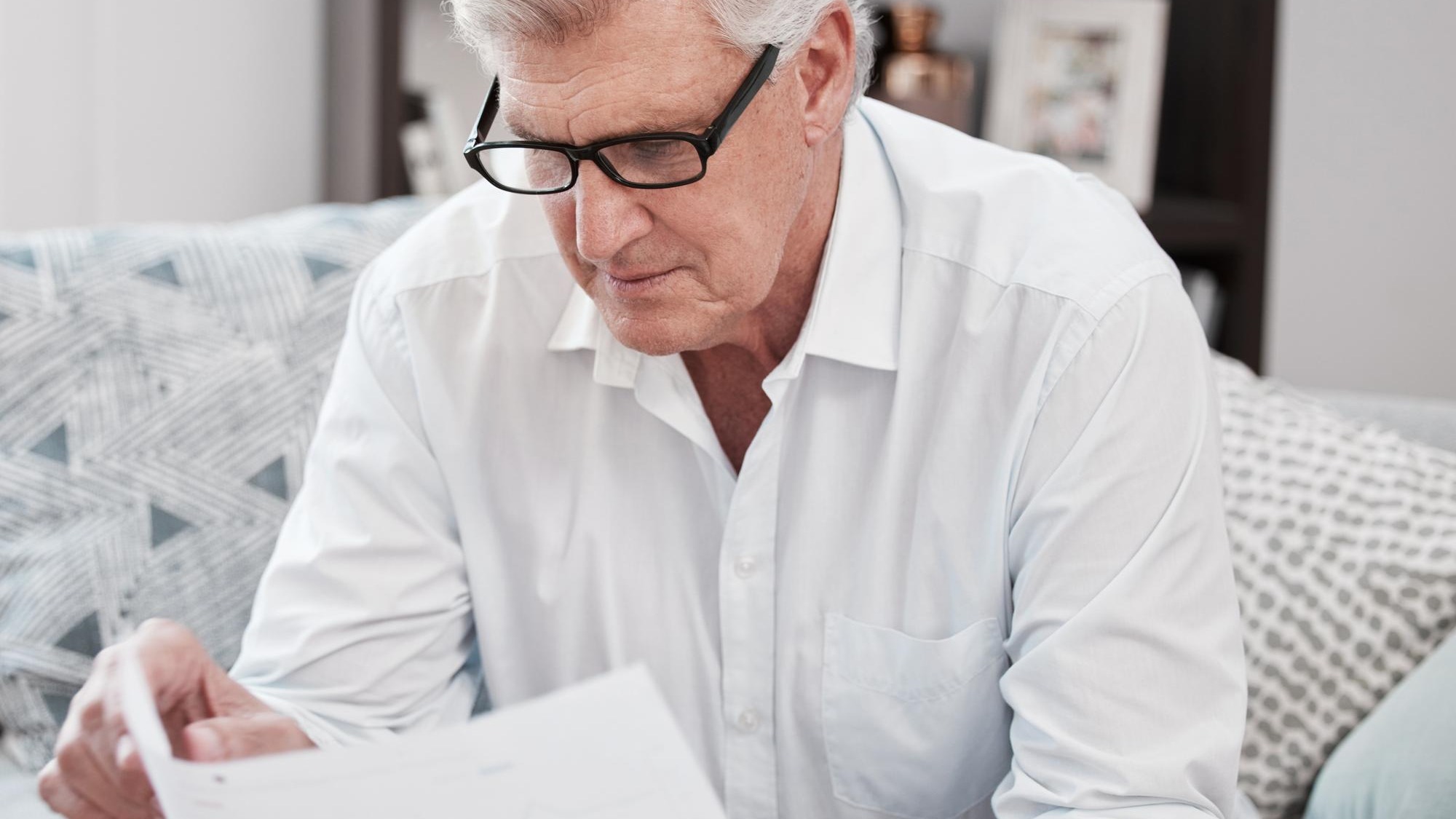 Document reading and senior man on sofa planning mortgage bills and debt payments at home Receipt saving and elderly male person with finance paperwork for pension fund in living room at house