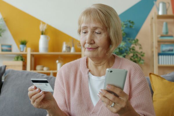 Elderly woman holding credit card and smartphone.