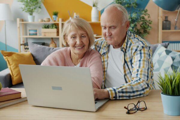 Elderly couple smiling while looking at laptop together.